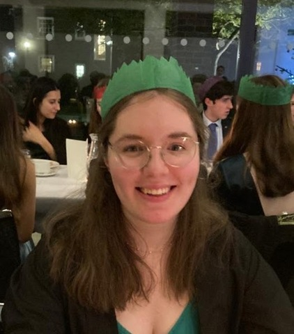 A photo of Sally smiling at a formal. She has long brown hair and glasses, and is wearing a green Christmas cracker crown.